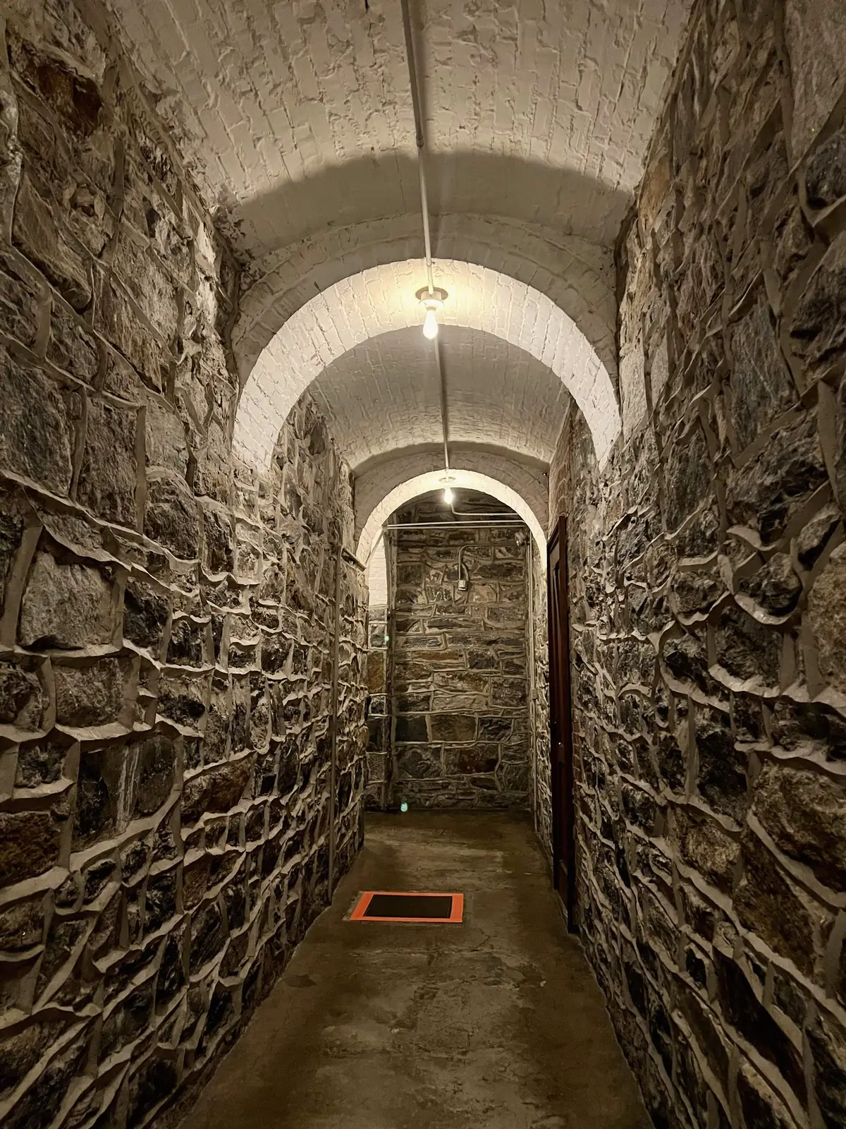 Cave voûtée aux murs de pierre, couloir étroit qui file vers la lumière